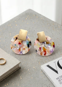Multicolored round earrings with gold posts on a gray stand.