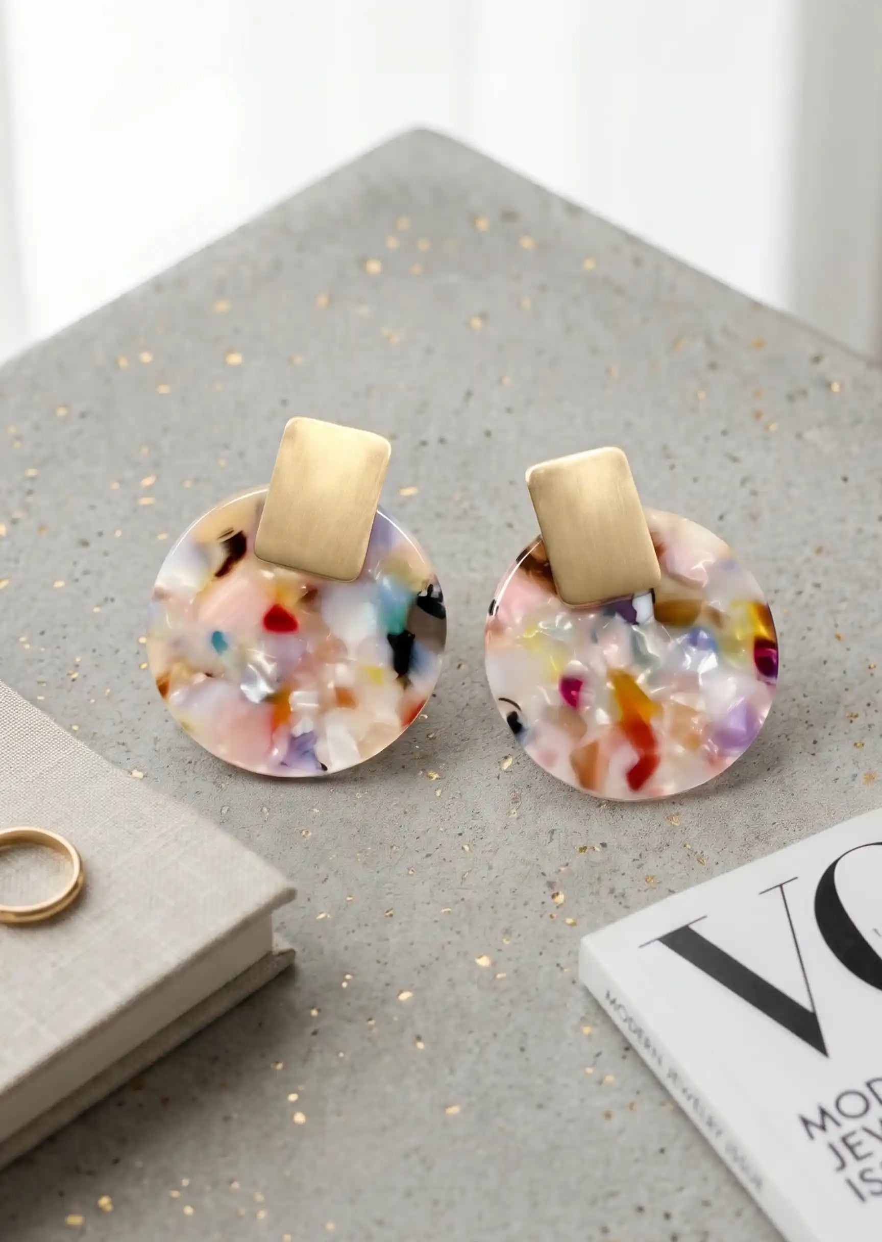 Multicolored round earrings with gold posts on a gray stand.