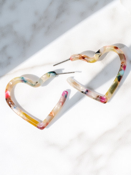 Two heart shaped hoop earrings with a white base and multi-colored swirls of red, pink, blue, yellow, green, and brown.