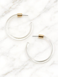 Pair of clear Lucite hoop earrings by Bauble Sky featuring polished transparent resin, gold-tone accents, and a modern minimalist design.