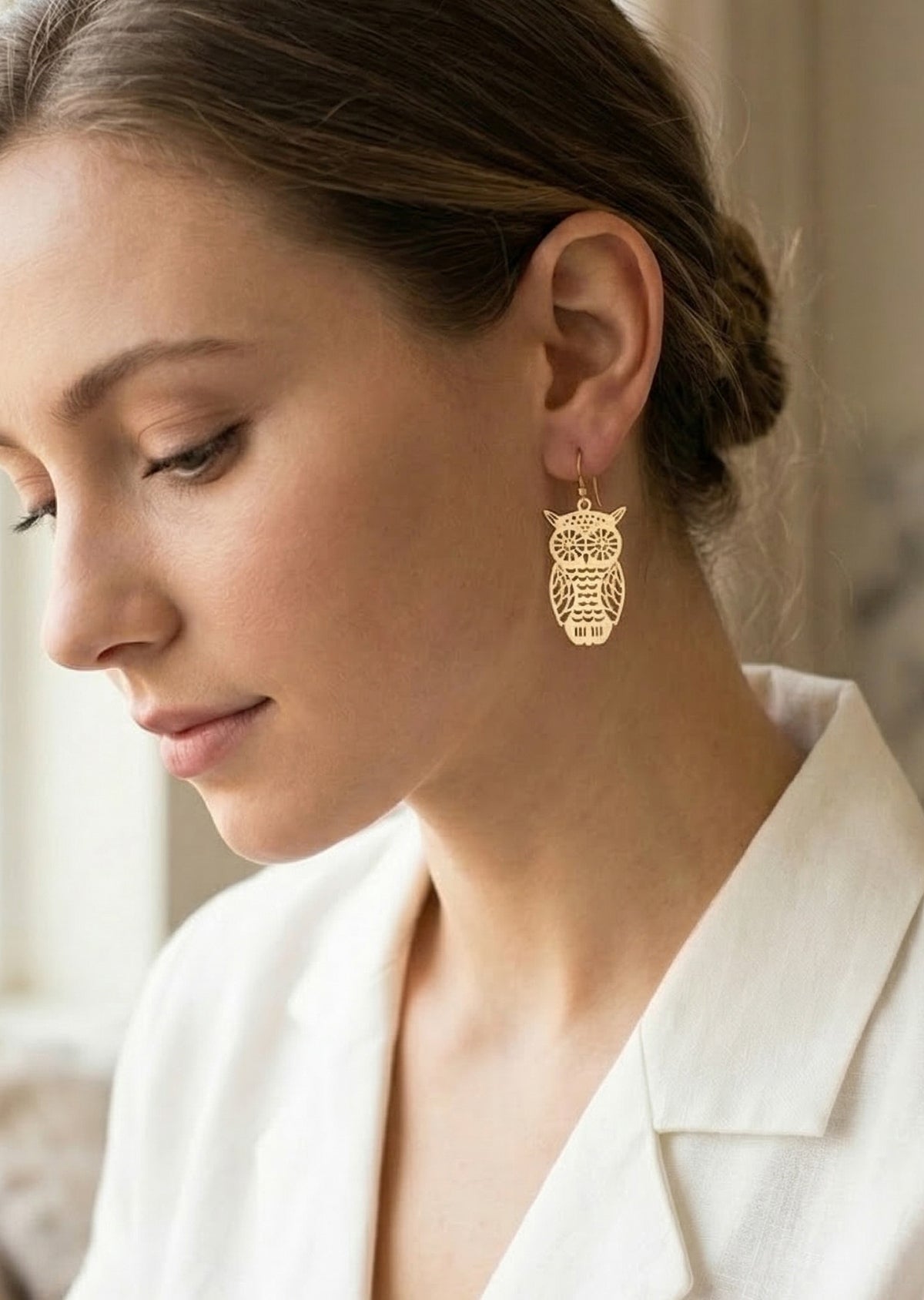 Woman wearing gold owl earrings with a neutral background