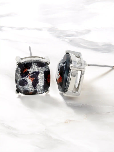 A pair of silver stud earrings with square cushion-cut black and white marbled gemstone centers, displayed on a white marble surface.