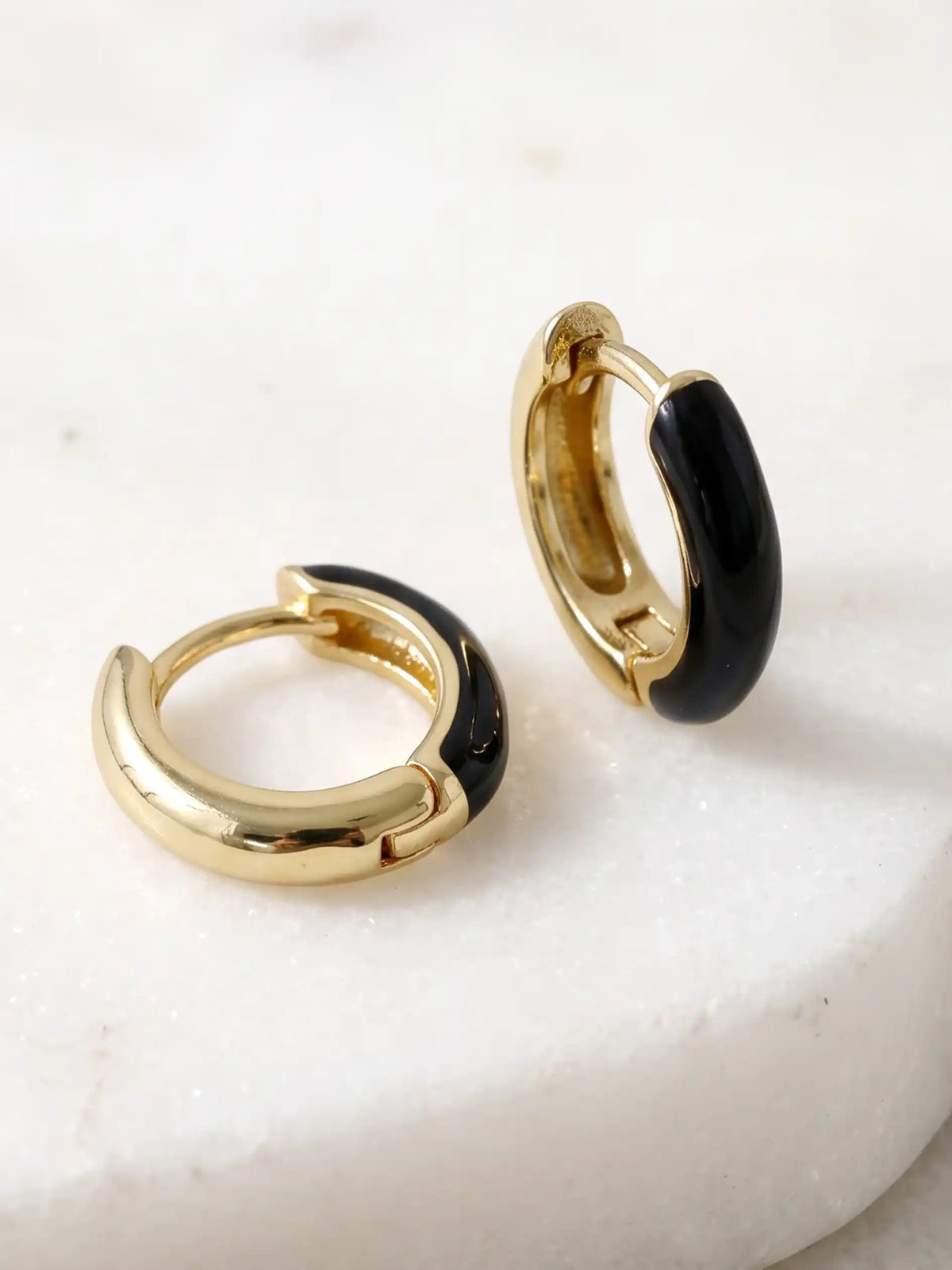 A pair of small gold-plated huggie hoop earrings featuring contrasting colorful black epoxy accents in a modern, compact design.