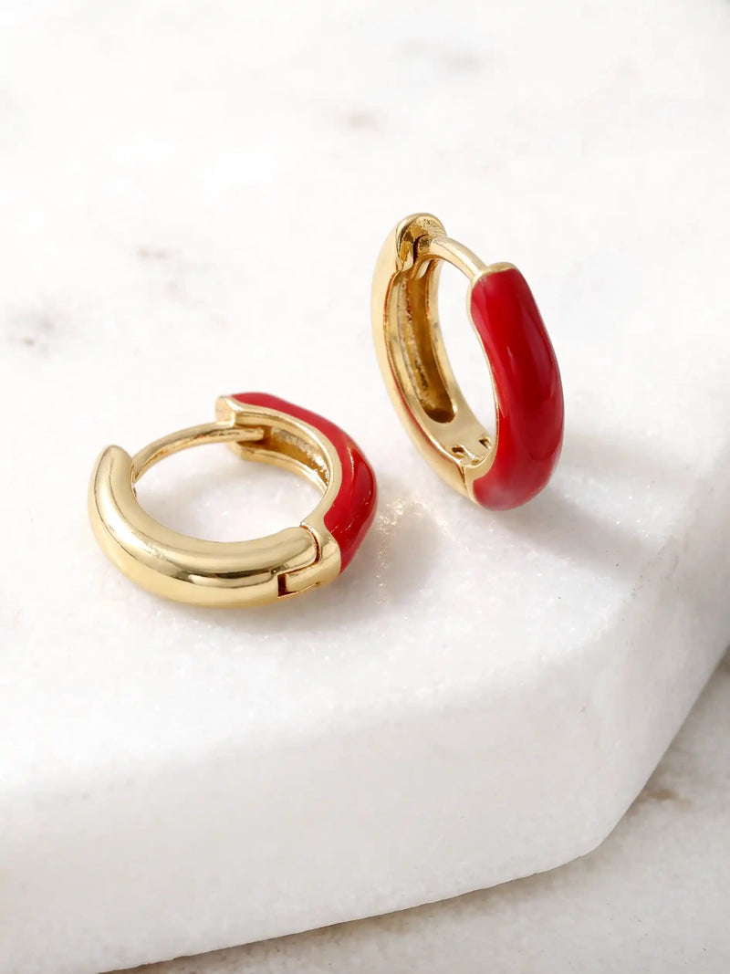 A pair of small gold-plated huggie hoop earrings featuring contrasting colorful red epoxy accents in a modern, compact design.