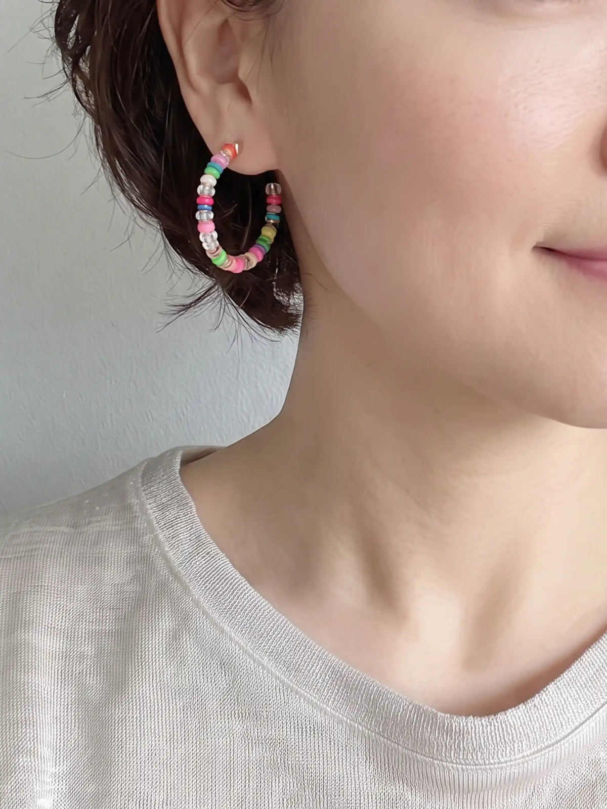 A close-up of a pair of lightweight clear glass beaded hoop earrings with multicolored rubber bead accents and gold-tone details by Bauble Sky.