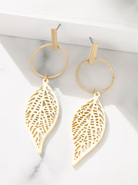 Gold leaf-shaped earrings on a white surface