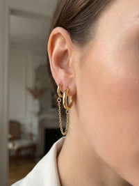 Close-up of a person wearing gold hoop earrings with a blurred indoor background
