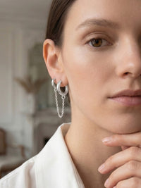 Close-up of a woman wearing silver hoop earrings with a blurred indoor background