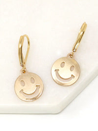 A pair of gold smiley face drop earrings with leverback hooks, displayed on a white textured surface.