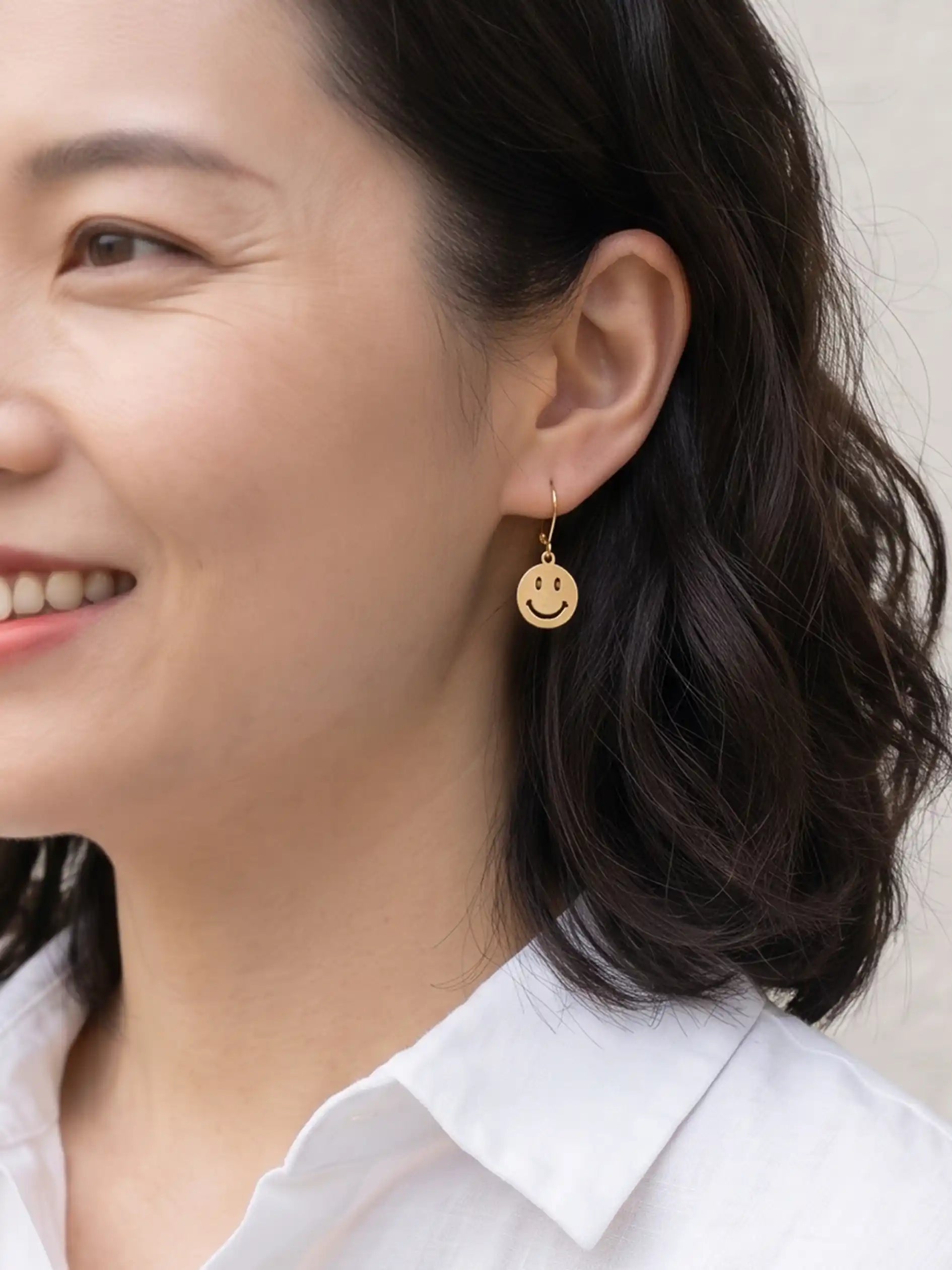 A pair of gold smiley face drop earrings with leverback hooks.