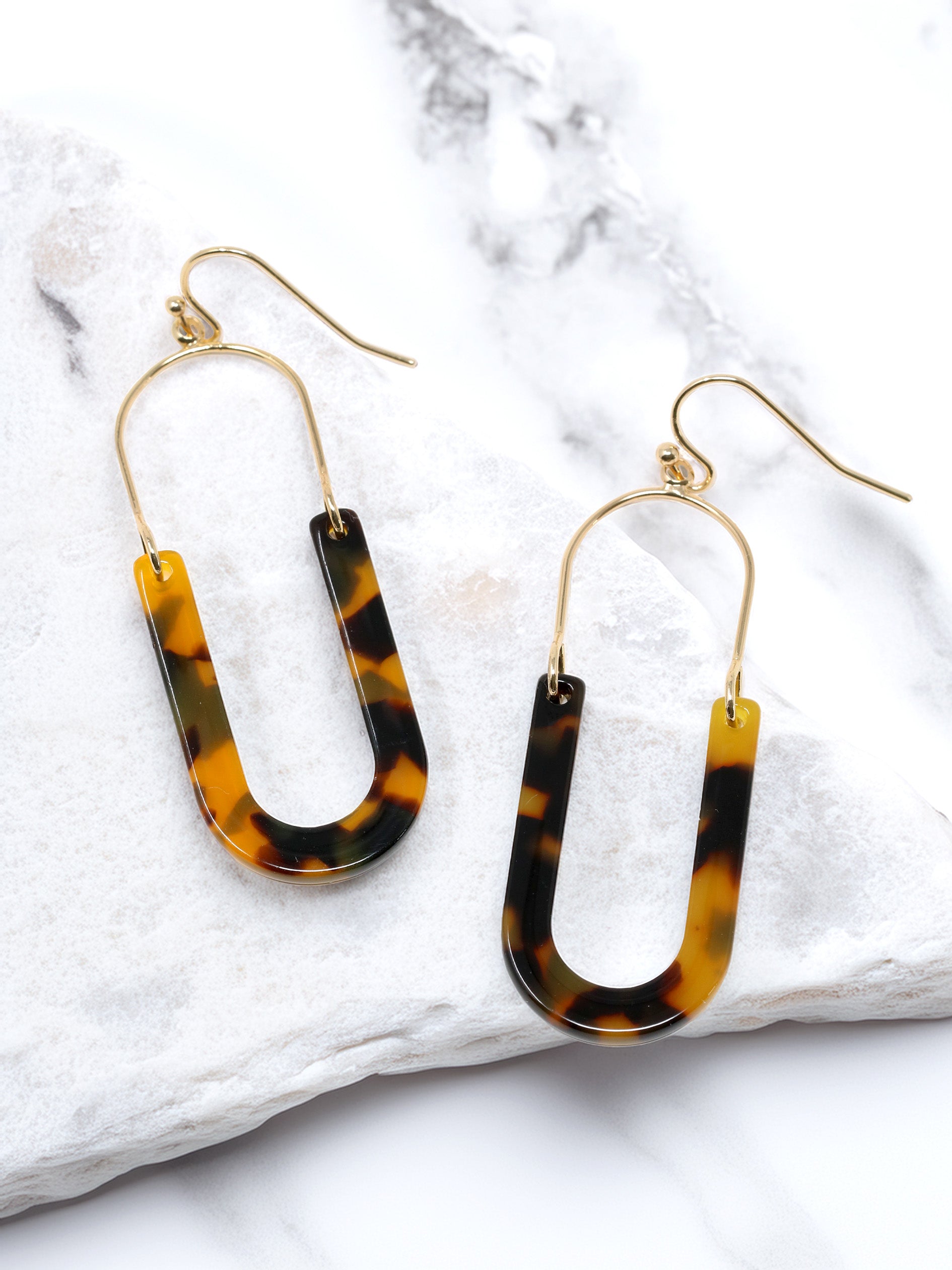 A pair of oval resin drop and dangle earrings with gold-tone hooks and frames. The U-shaped resin pendants feature a brown tortoise tones.