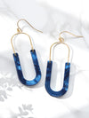 A pair of oval resin drop and dangle earrings with gold-tone hooks and frames. The U-shaped resin pendants feature a brown blue tones.
