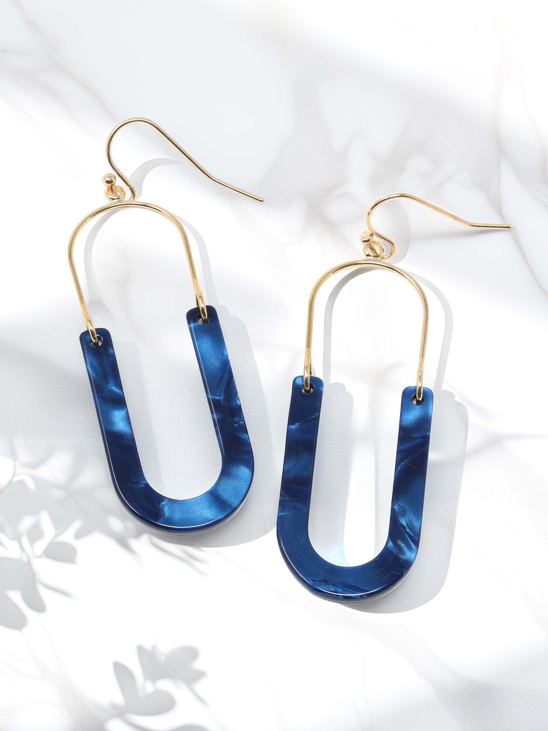 A pair of oval resin drop and dangle earrings with gold-tone hooks and frames. The U-shaped resin pendants feature a brown blue tones.