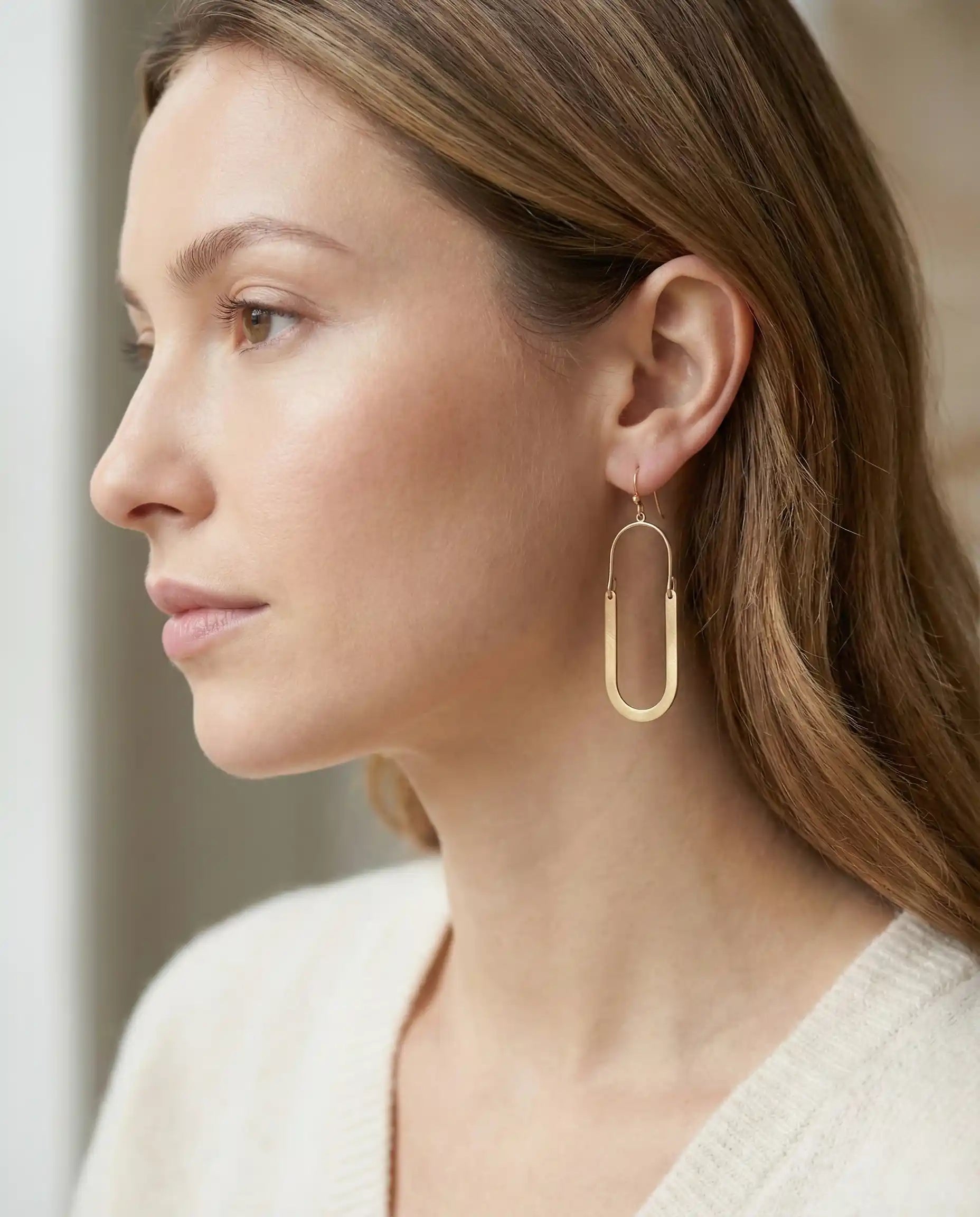 Woman wearing gold tone U-shaped dangle earrings with gold-tone hooks, paired with a moss green knit sweater.