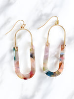 A pair of oval resin drop and dangle earrings with gold-tone hooks and frames. The U-shaped resin pendants feature a multicolored, marbled design in soft pastel and vibrant hues, including pink, blue, green, and peach.