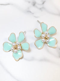 Light blue flower-shaped earrings with pearl centers on a marble background