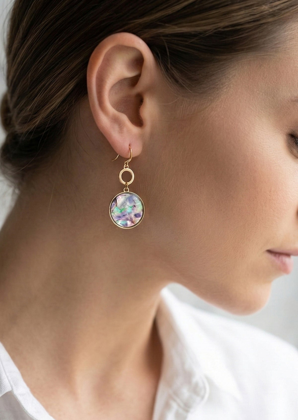Close-up of a woman wearing a gold earring with a colorful gemstone.
