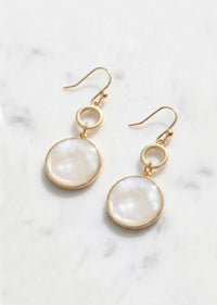 Gold earrings with round white stones on a marble surface