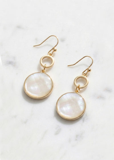 Gold earrings with round white stones on a marble surface