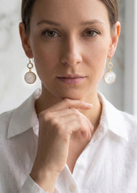 Woman wearing pearl earrings with a white shirt against a neutral background