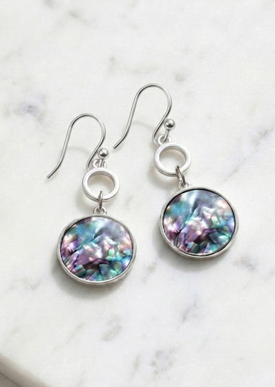 Pair of earrings with colorful round stones on a marble background