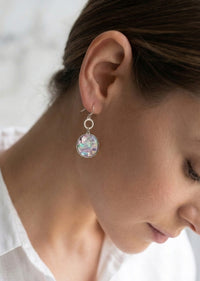 Close-up of a person wearing a silver earring with a colorful gemstone.