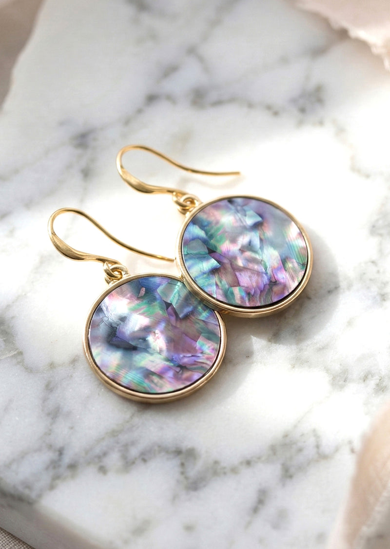 Gold earrings with colorful round stones on a marble surface