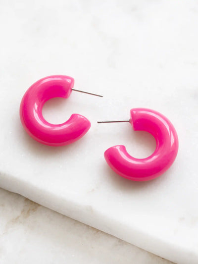 A pair of neon pink colored resin hoop earrings with a bold rounded 25mm design.