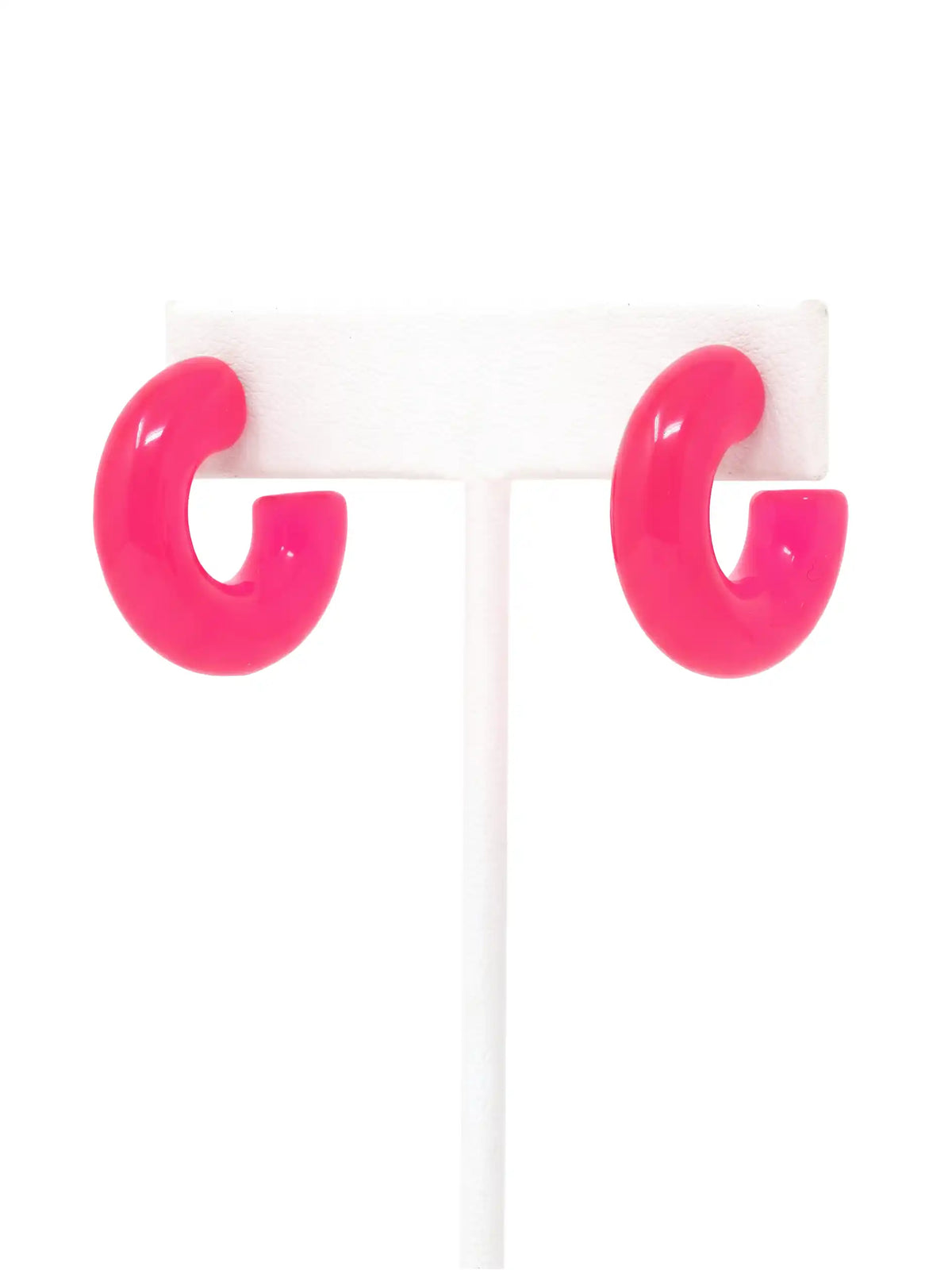 A pair of neon pink colored resin hoop earrings with a bold rounded 25mm design.