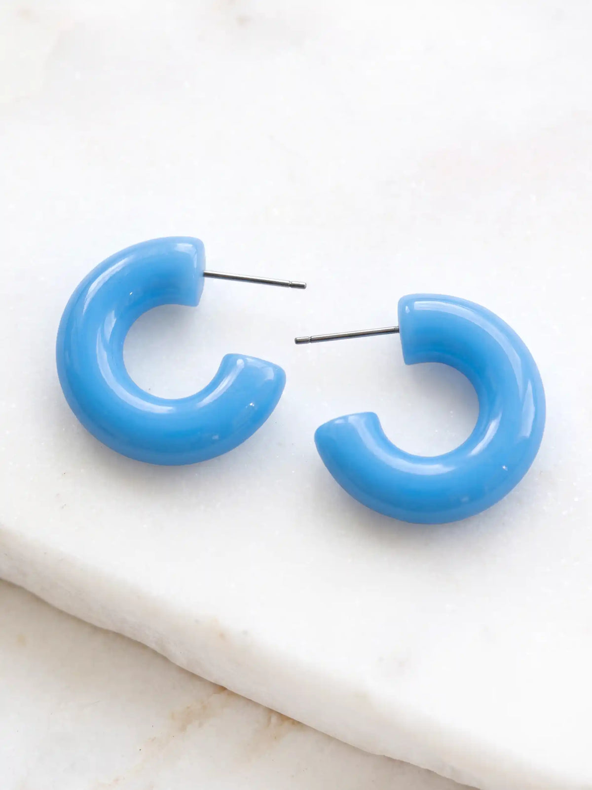 A pair of tranquil blue colored resin hoop earrings with a bold rounded 25mm design.