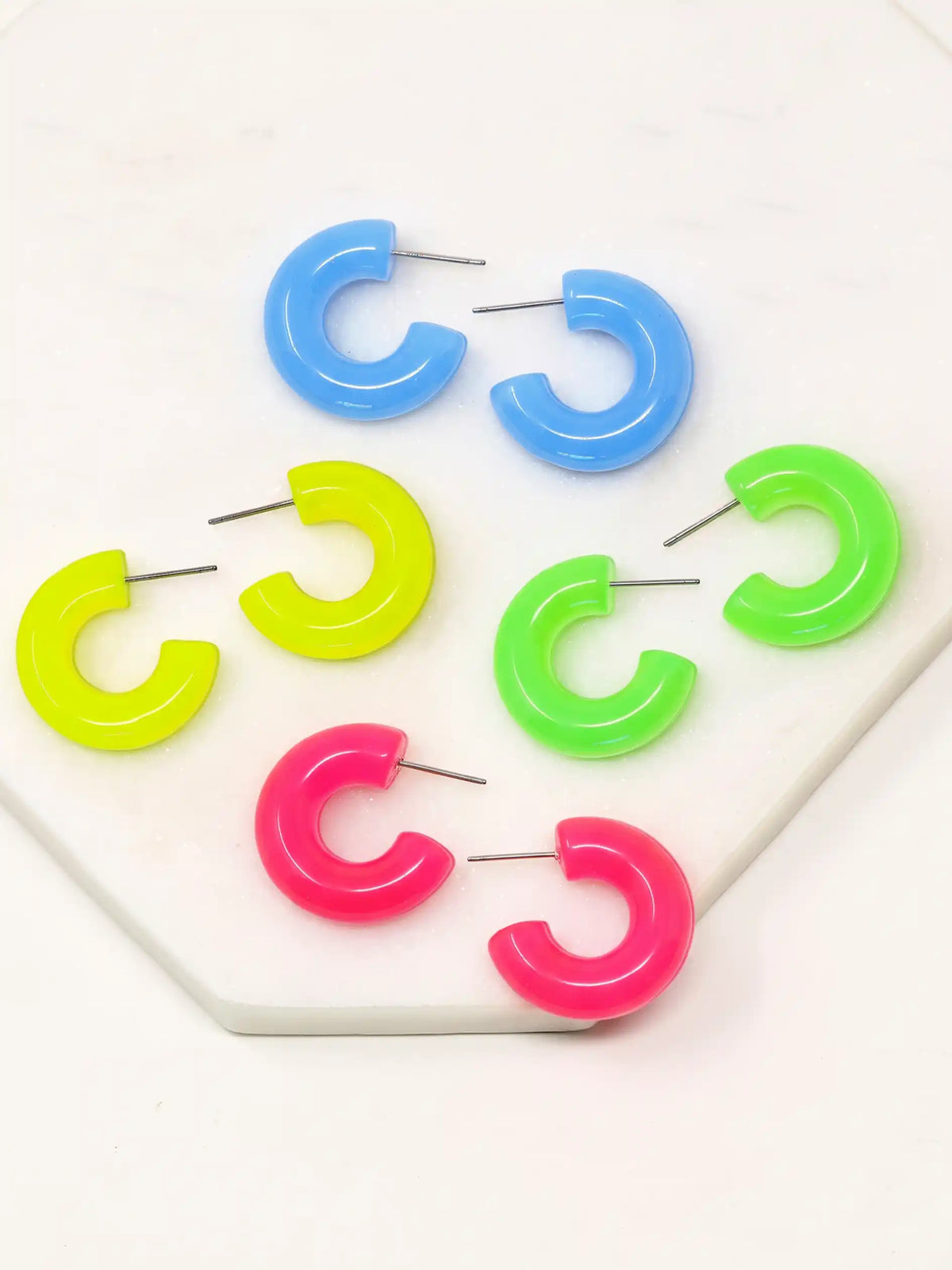 Pair of neon colored resin hoop earrings with a bold rounded 25mm design, available in vibrant pink, yellow, green, and tranquil blue, by Bauble Sky.