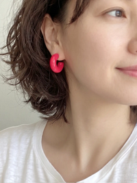 A pair of neon pink colored resin hoop earrings with a bold rounded 25mm design.