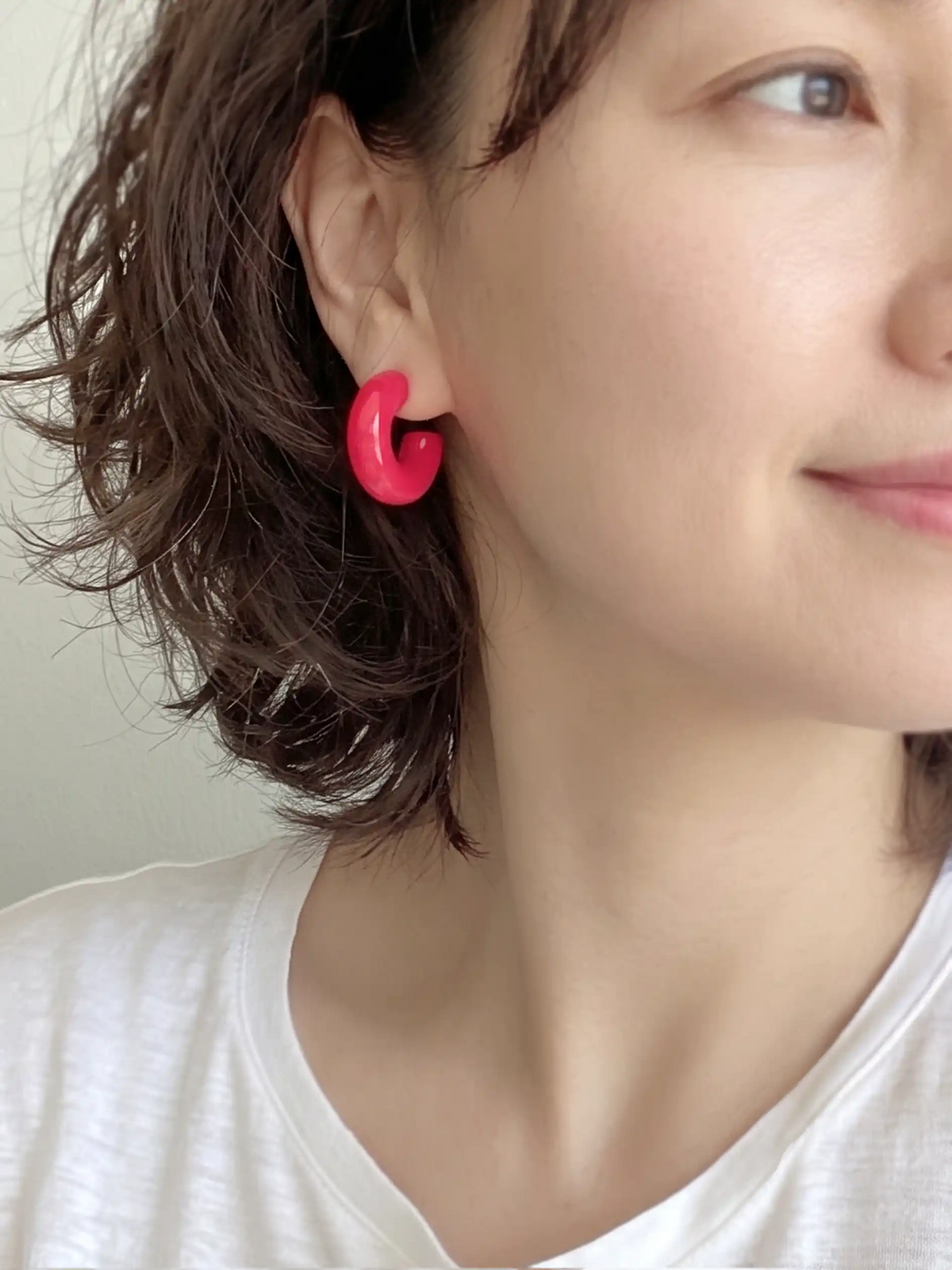 A pair of neon pink colored resin hoop earrings with a bold rounded 25mm design.