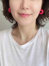 A pair of neon pink colored resin hoop earrings with a bold rounded 25mm design.