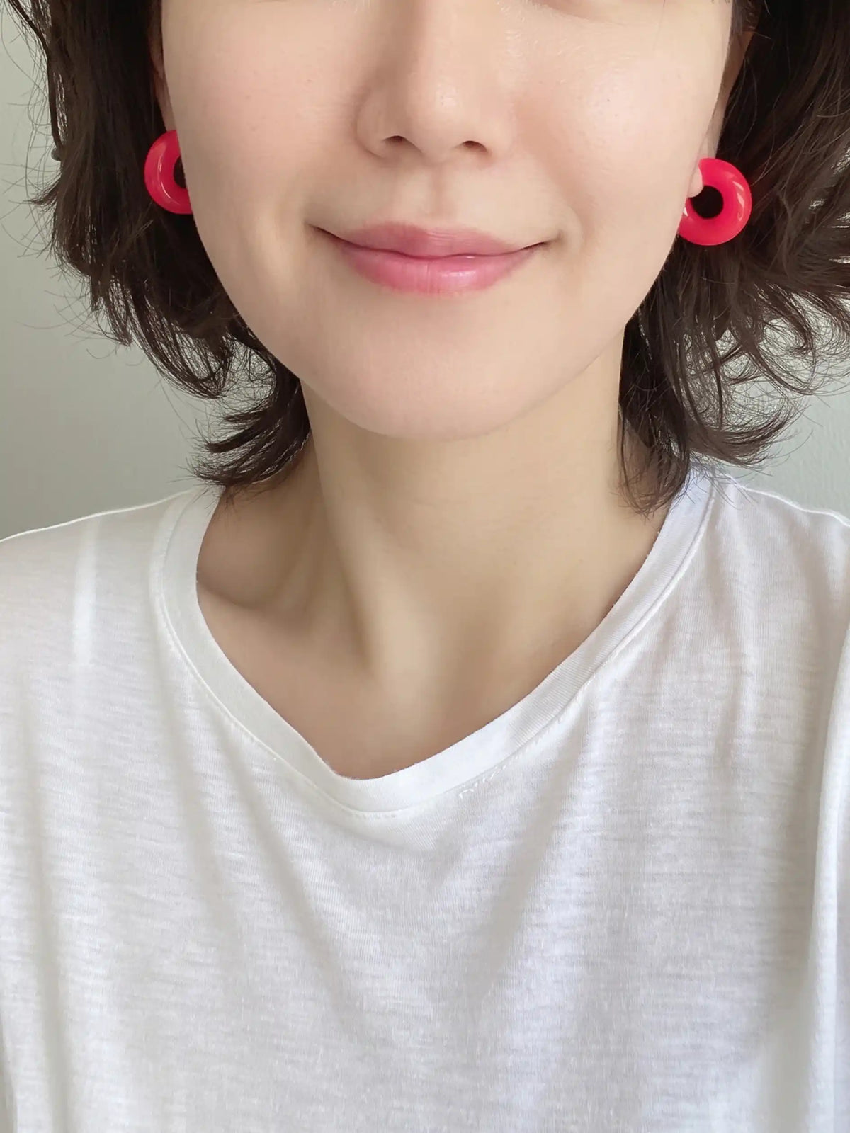 A pair of neon pink colored resin hoop earrings with a bold rounded 25mm design.