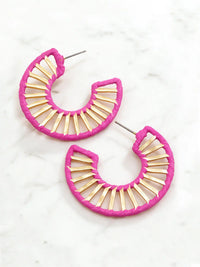 A pair of crescent-shaped hoop earrings with a bright pink textured outer border and gold-toned inner bars, displayed on a light marble surface.