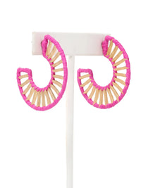A pair of large crescent-shaped hoop earrings with bright pink wrapped edges and natural wood slats inside, displayed on a white stand against a white background.