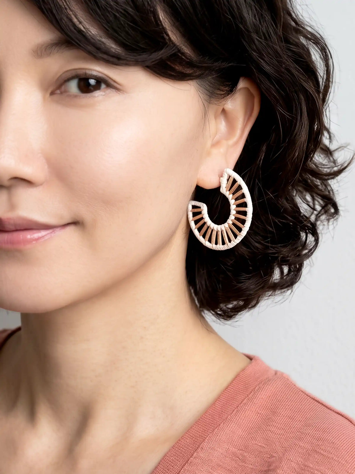 A close-up of a woman wearing a large, gold-toned crescent-shaped hoop earring with a sunburst or fan-like cutout pattern.