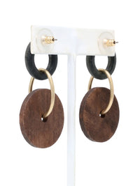 A pair of dangling earrings hanging side-by-side on a white T-bar jewelry display stand, shown against a bright white background. Each earring features a small, textured black ring at the top, which is connected to a larger, flat, brown circular wooden disc by a matte-gold metallic hoop that passes through the disc's center hole. A small gold-tone stud fixture loops over the top of each black ring