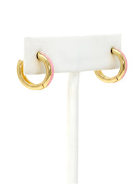 A close-up of a pair of 15mm gold-plated huggie hoop earrings with a light pink epoxy color accent on one side.