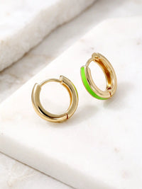 A close-up of a pair of 15mm gold-plated huggie hoop earrings with a neon green epoxy color accent on one side.