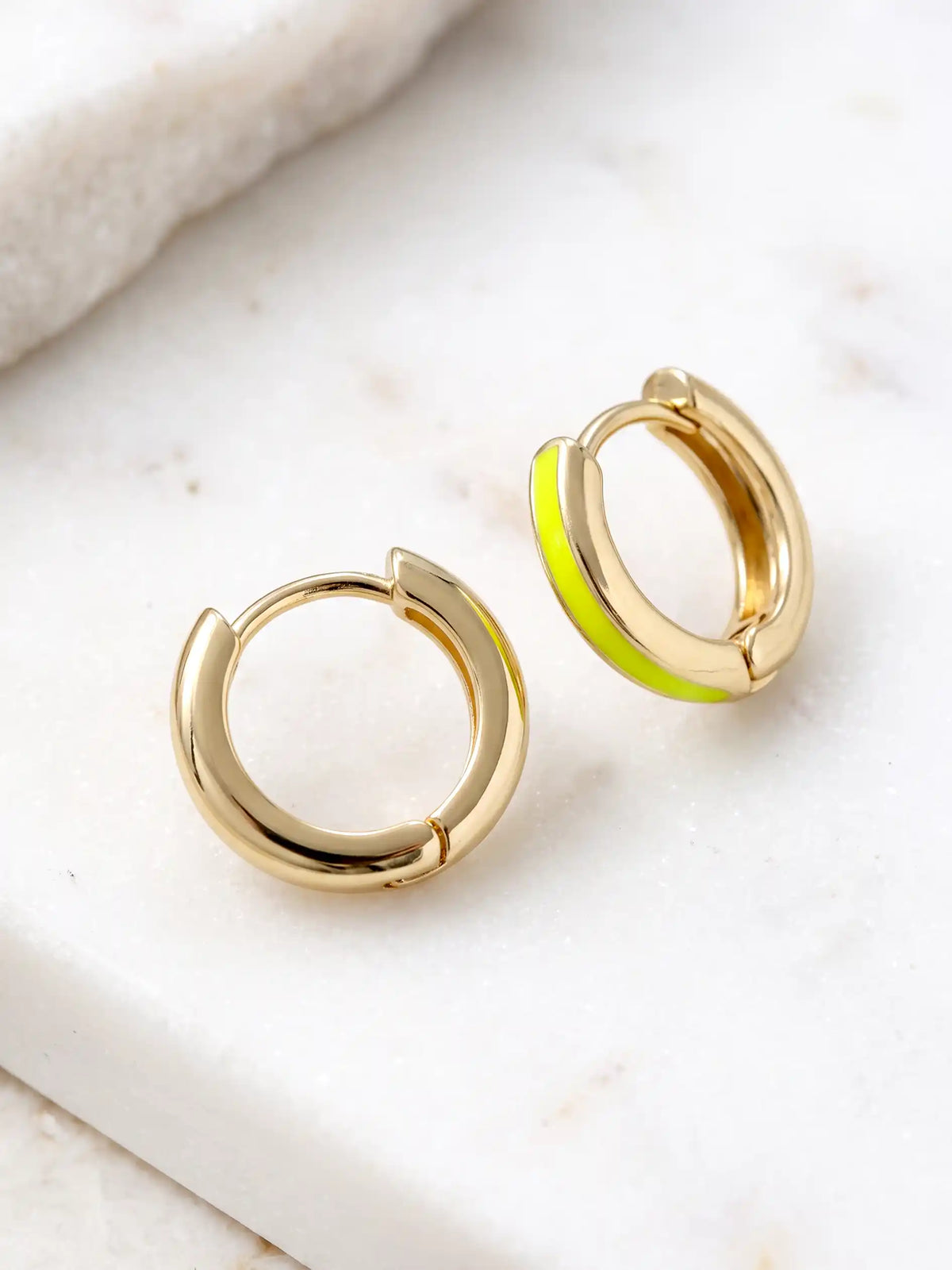 A close-up of a pair of 15mm gold-plated huggie hoop earrings with a  neon yellow epoxy color accent on one side.
