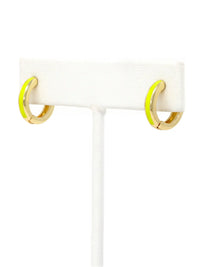 A close-up of a pair of 15mm gold-plated huggie hoop earrings with a  neon yellow epoxy color accent on one side.