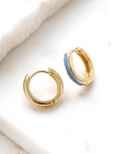 A close-up of a pair of 15mm gold-plated huggie hoop earrings with a tranquil blue epoxy color accent on one side.