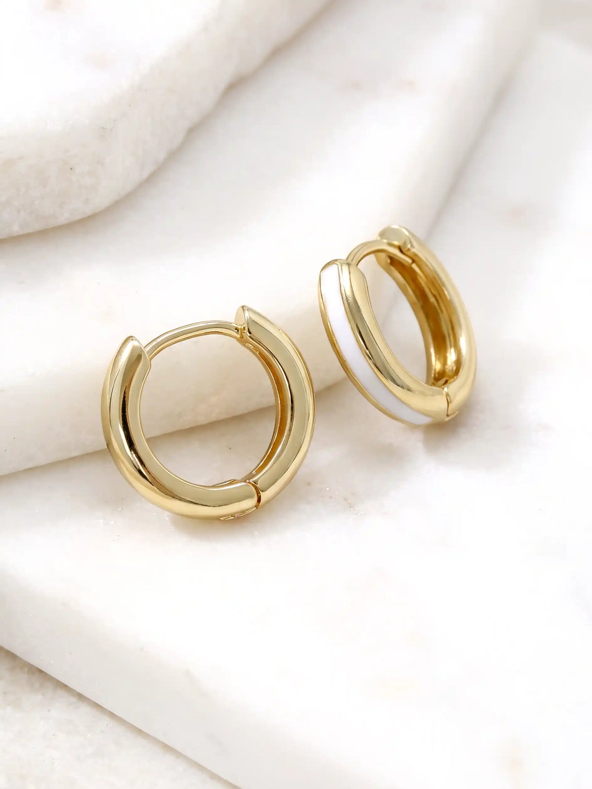 A close-up of a pair of 15mm gold-plated huggie hoop earrings with a white epoxy color accent on one side.