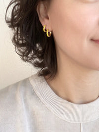 A close-up of a pair of 15mm gold-plated huggie hoop earrings with a  neon yellow epoxy color accent on one side.