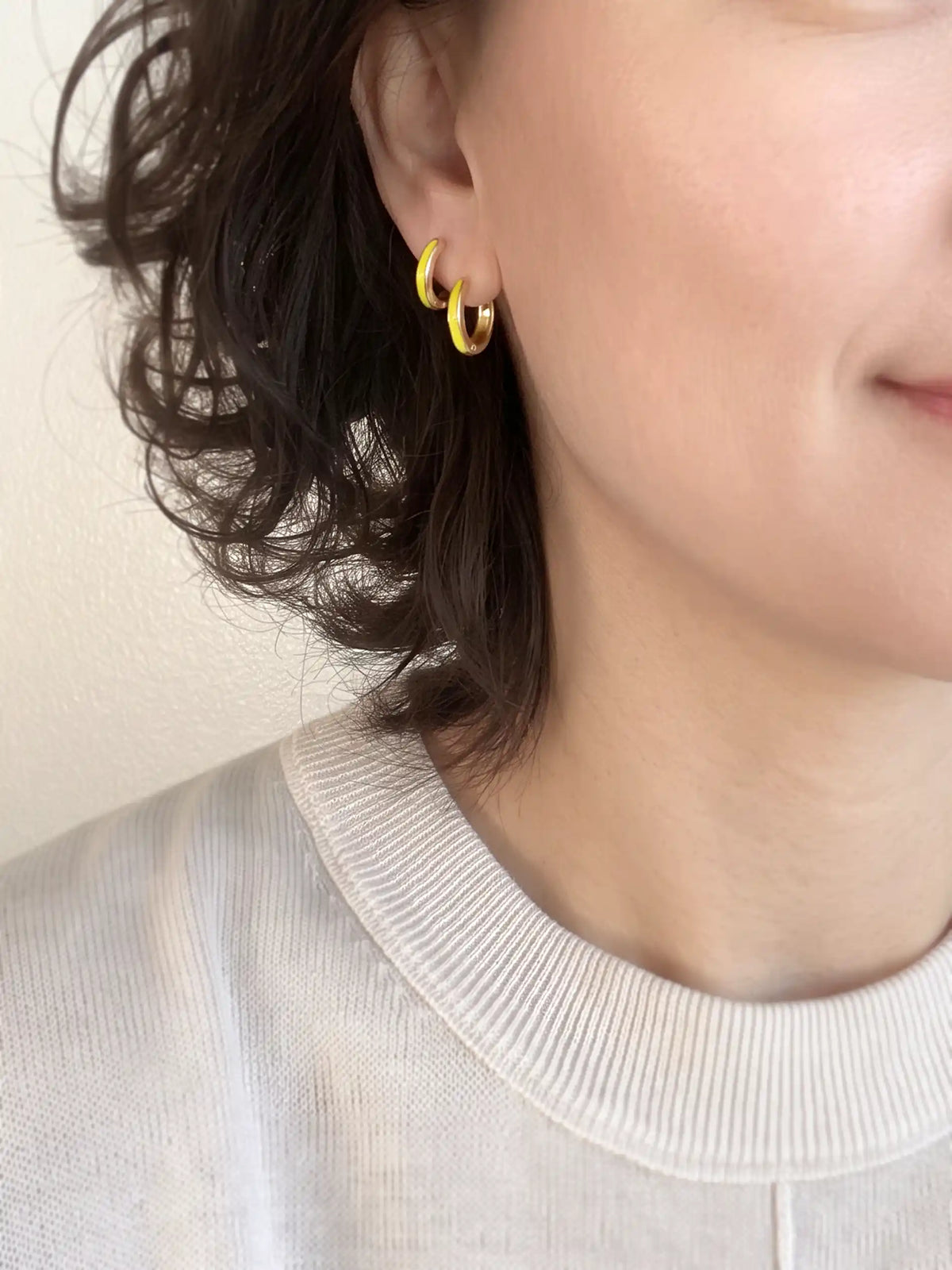 A close-up of a pair of 15mm gold-plated huggie hoop earrings with a  neon yellow epoxy color accent on one side.