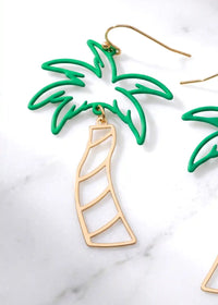 A pair of cutout palm tree drop earrings featuring bright green palm leaves and a gold-tone trunk, dangling from gold hook backings.