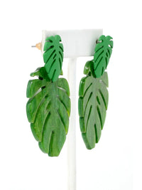 A pair of resin green leaf-shaped drop earrings displayed on a white stand against a white background.
