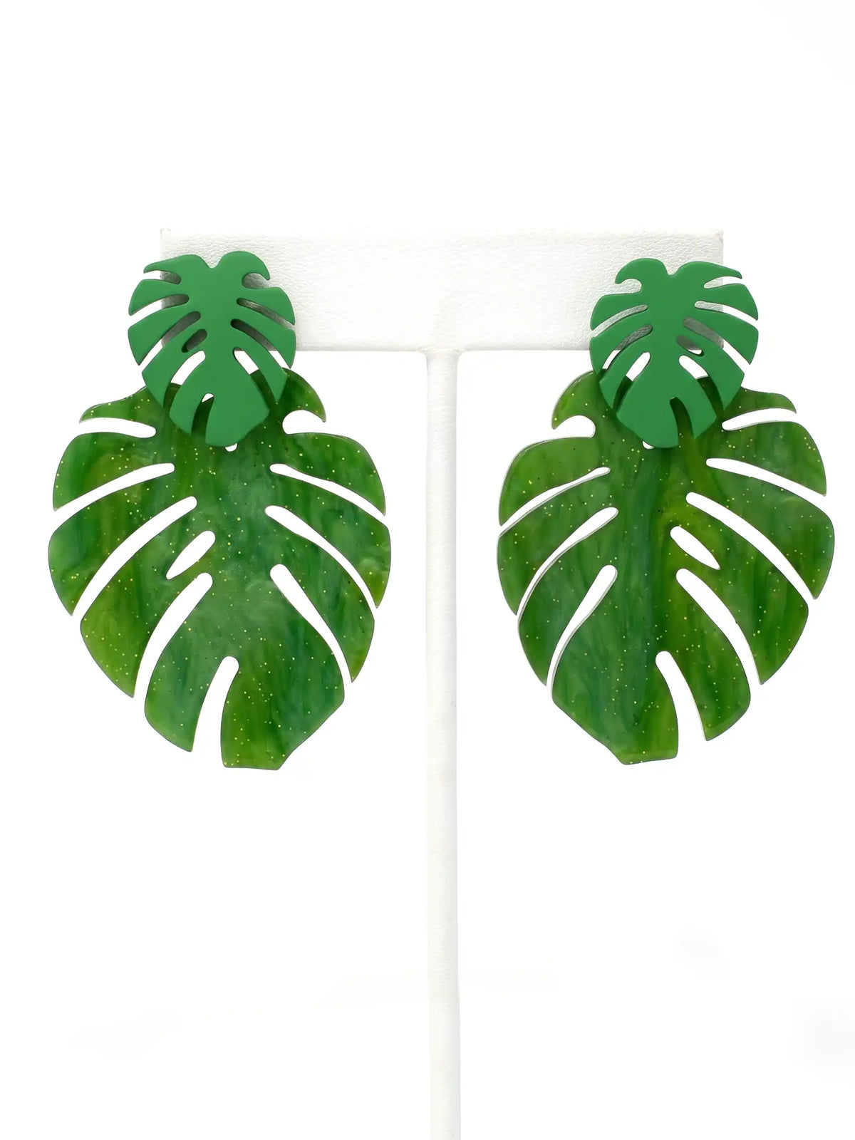 A pair of green monstera leaf stud earrings displayed on a white T-stand against a white background.